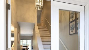 A modern interior with a staircase leading to a second floor, a dining area with a table and chairs, and a decorative wall piece.