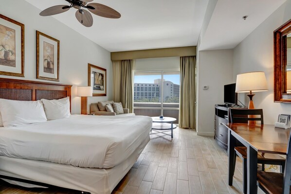 A hotel room with a large bed, a desk, a chair, a TV, and a window with curtains.