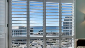 Habitación con un amplio ventanal con persianas horizontales, vista al océano y un estacionamiento debajo.