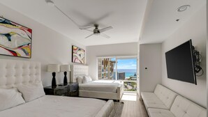 Et moderne hotelværelse med en stor seng, to mindre senge, en sofa, en loftsvifte og et fjernsyn.