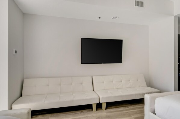 Un salon moderne avec un canapé blanc, un téléviseur à écran plat fixé au mur et un plancher en bois.