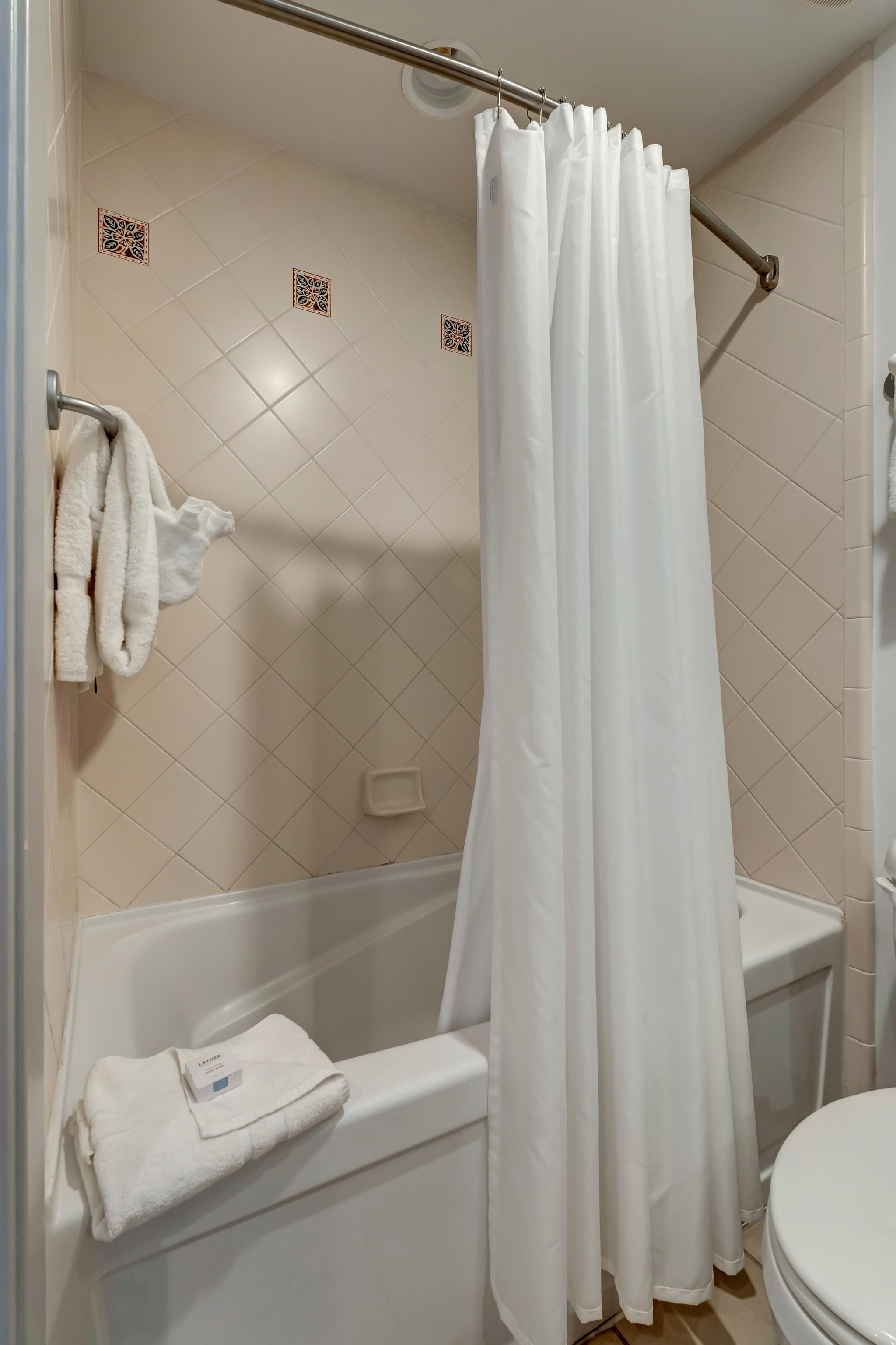 A bathroom with a bathtub, a shower curtain, and a toilet.