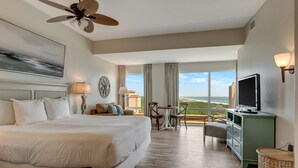 A hotel room with a large bed, a ceiling fan, a TV, a dining table with chairs, and a view of the ocean. - Amazing Views: King Bed, Sleeper Sofa, Kitchenette, Sleeps 3 at Sandestin Golf and Beach Resort! (Miramar Beach)