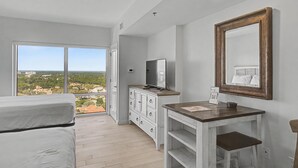 Et soveværelse med balkon, kommode, fjernsyn og spejl.