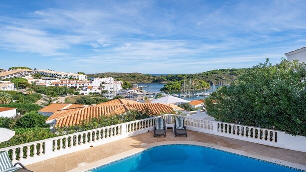 A pool area with a view of a coastal town, including buildings and boats. - Villa Alma del Mar - Exceptional Villa with Marina Views & Pool (Minorca)