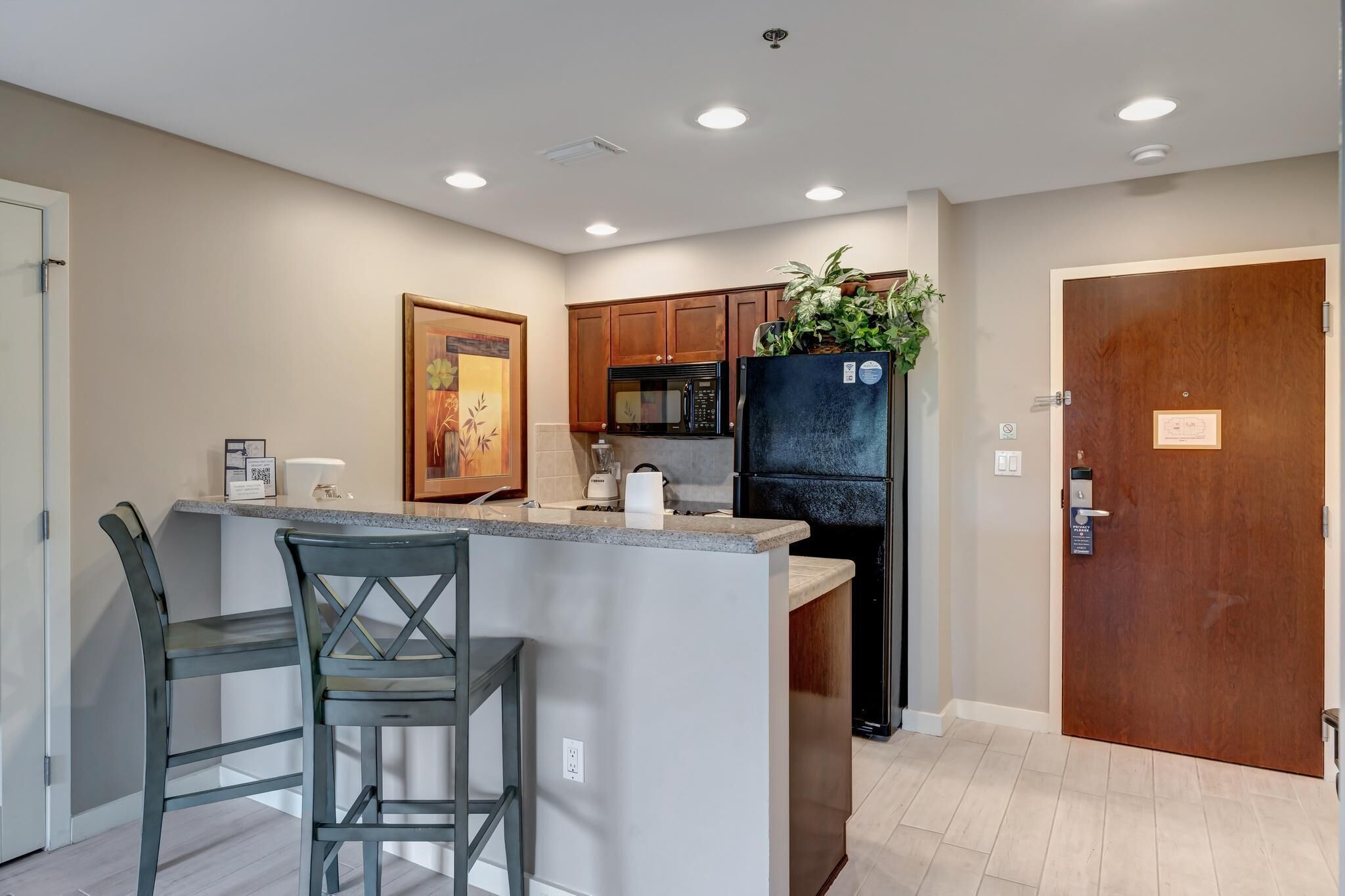 A kitchen with a central island, wooden cabinets, a refrigerator with a plant, and a door with a plaque.