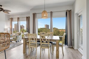 Ein Essbereich mit Holztisch und -stühlen, großen Fenstern mit Vorhängen und Blick auf Gebäude und Bäume.