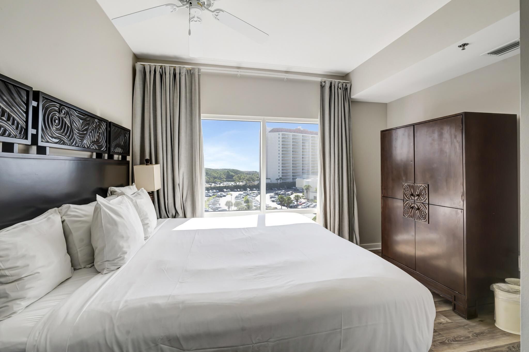 A hotel room with a large bed, a wardrobe, and a view of a cityscape through a large window.