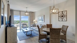 Ein modernes Wohnzimmer mit einer Couch, einem Esstisch, Korbstühlen, einem Couchtisch und einem Fernseher auf einer Holzkommode.