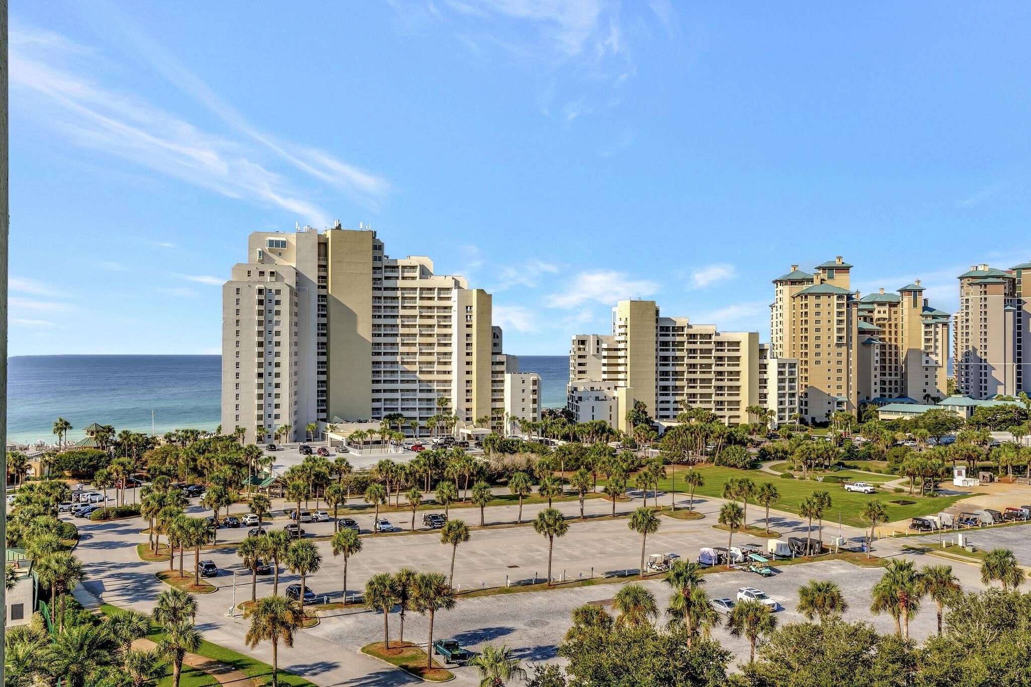 A high-rise hotel complex with multiple buildings, a parking area, and a view of the ocean.
