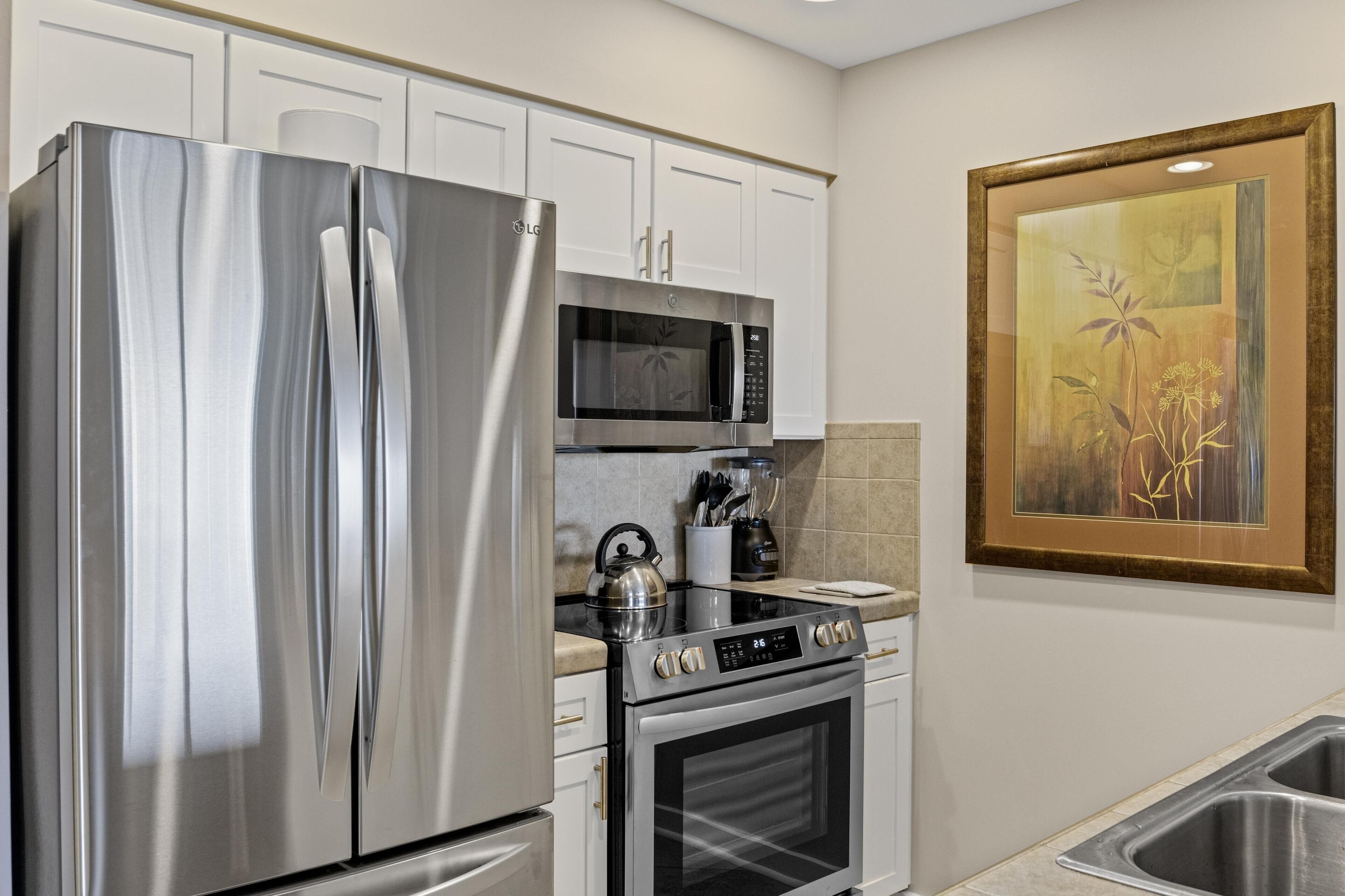 A modern kitchen with stainless steel appliances, white cabinetry, and a framed artwork on the wall.
