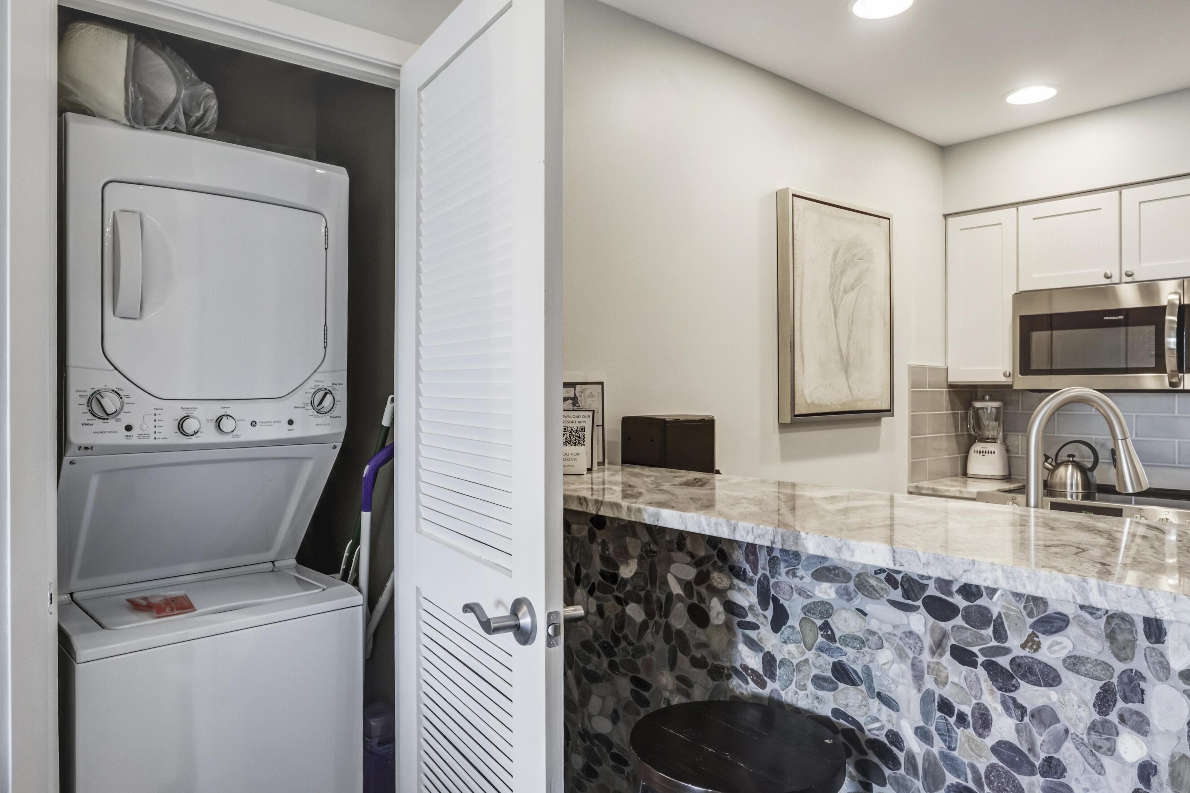 A laundry room with a washing machine and dryer, a kitchen with granite countertops and stainless steel appliances, and a stone backsplash.