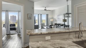 A modern hotel room with a marble kitchen island, a dining area with a table and chairs, and a balcony with curtains. - Luau 1BR Gem: Ocean Views, Lagoon Pool, Tiki Bar, Steps to Sandestin Beach (Miramar Beach)