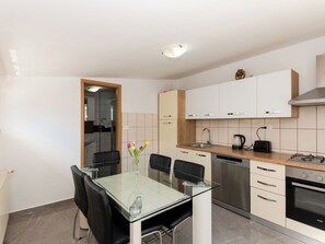 Una cocina moderna con una mesa de comedor de vidrio, sillas negras, lavavajillas empotrado, estufa y armarios blancos.