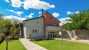 Une maison à deux étages, avec un chemin de pierre menant à l’entrée, entourée d’une pelouse bien entretenue et d’arbres.