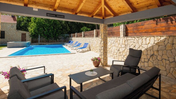 Un espace extérieur abrité comprenant une piscine, des chaises longues et un mur en pierre.