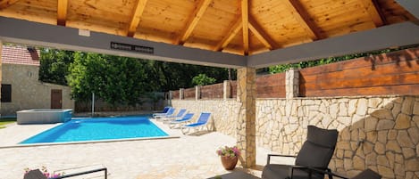 A covered outdoor area with a pool, lounge chairs, and a stone wall.