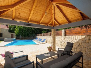 Ein überdachter Außenbereich mit Pool, Liegestühlen und einer Steinmauer.