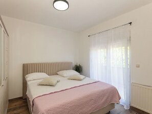 Un dormitorio con cama, ventana con cortinas translúcidas, radiador e iluminación en el techo.