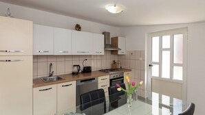 Une cuisine moderne avec des meubles blancs, une cuisinière à gaz, un lave-vaisselle et un coin repas comprenant une table et des chaises en verre.