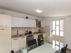 Una cocina moderna con armarios blancos, estufa a gas, lavavajillas y comedor con mesa y sillas de vidrio.