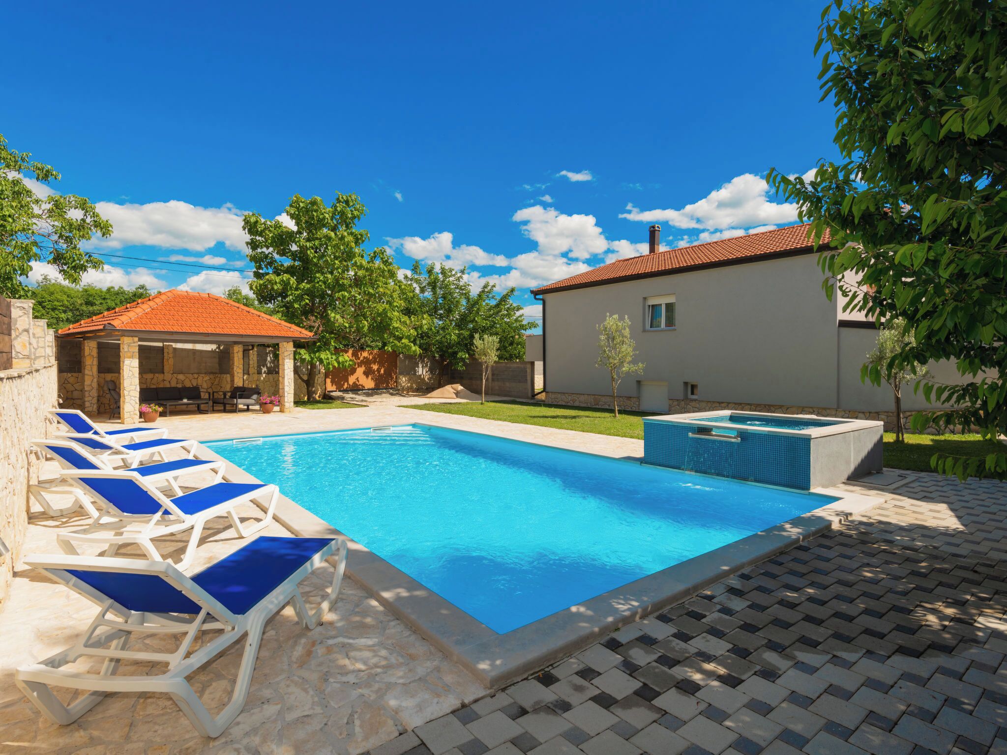A swimming pool with lounge chairs, a covered seating area, and a small building with a tiled roof.