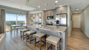 A modern kitchen with a large island, bar stools, and a view of the city. - Sandestin Escape: Spacious 2BR with Ocean Views, Poolside Bar, Resort Perks & More (Miramar Beach)