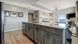 A modern kitchen with dark cabinetry, a marble countertop, and a large island. - Sandestin Escape: Spacious 2BR with Ocean Views, Poolside Bar, Resort Perks & More (Miramar Beach)