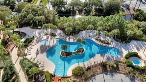 An aerial view of a resort with a large, winding pool surrounded by palm trees and lounge chairs. - Sandestin Escape: Spacious 2BR with Ocean Views, Poolside Bar, Resort Perks & More (Miramar Beach)