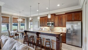 Una cocina amplia con armarios de madera, un refrigerador de acero inoxidable y una isla central con taburetes.