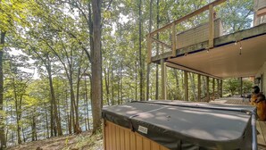 Een hottub op een houten terras met uitzicht op een bos en een meer.