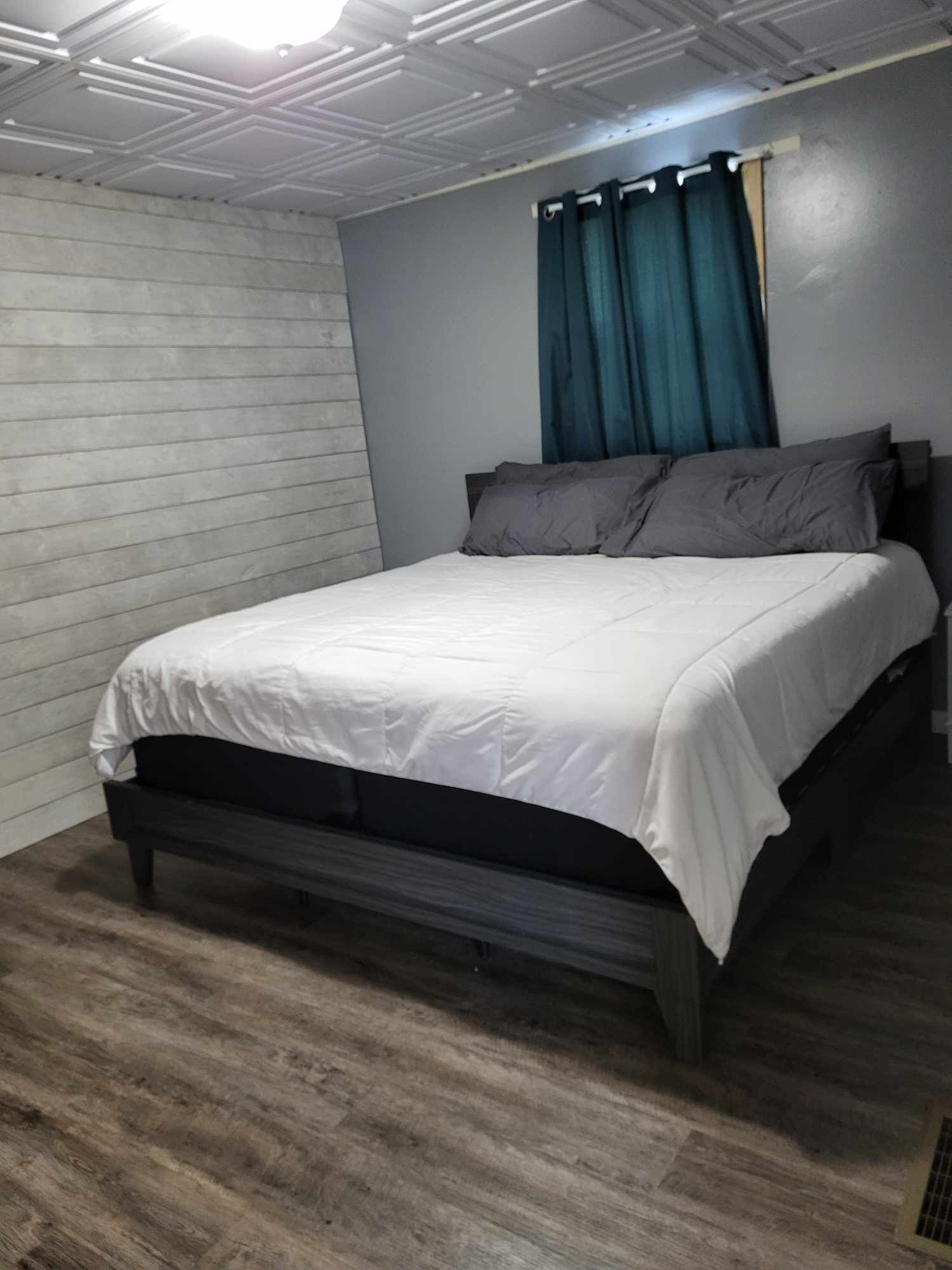 A bedroom with a bed, wooden flooring, a white wall, and a ceiling with recessed lighting.