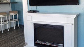 A modern living room with a fireplace, a mounted TV, and two bar stools.