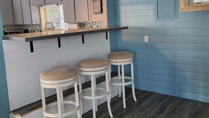 A kitchen with a bar area, wooden stools, and a window.