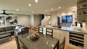 Une cuisine moderne dotée d’un îlot central, un coin repas avec une table en bois et un salon avec un canapé et un ventilateur de plafond.