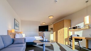 Quarto de hotel moderno com sofá, cama, mesa redonda pequena, televisão, armário de madeira e escrivaninha com cadeira.