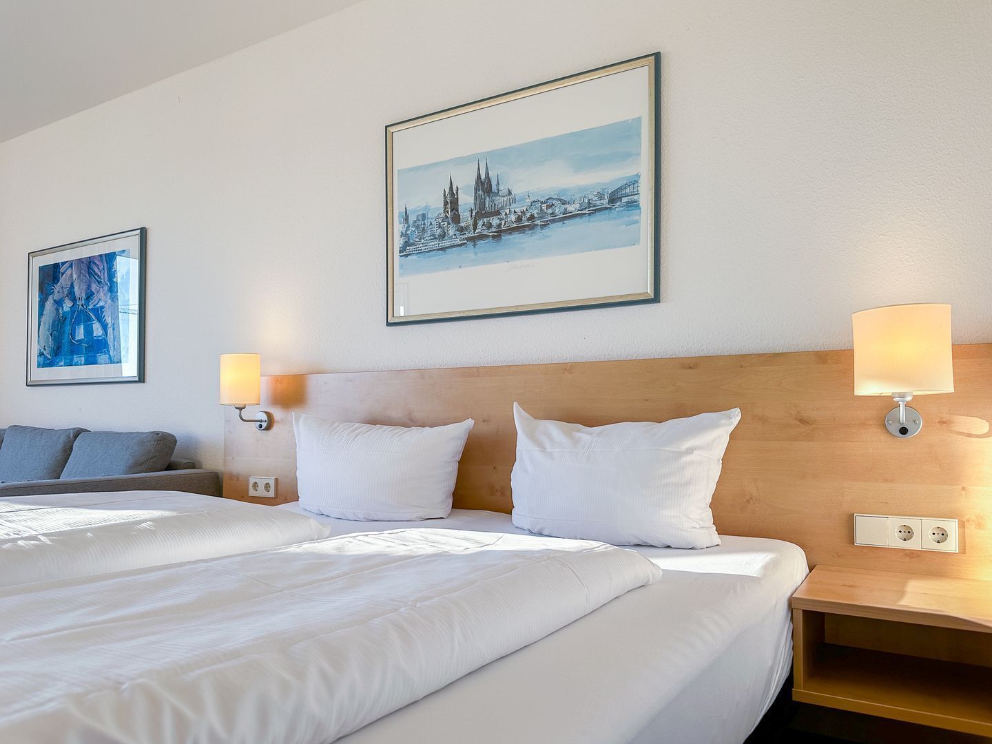 Una habitació d'hotel amb un llit gran, dues làmpades de nit, un capçal de llit i dues imatges emmarcades a la paret.