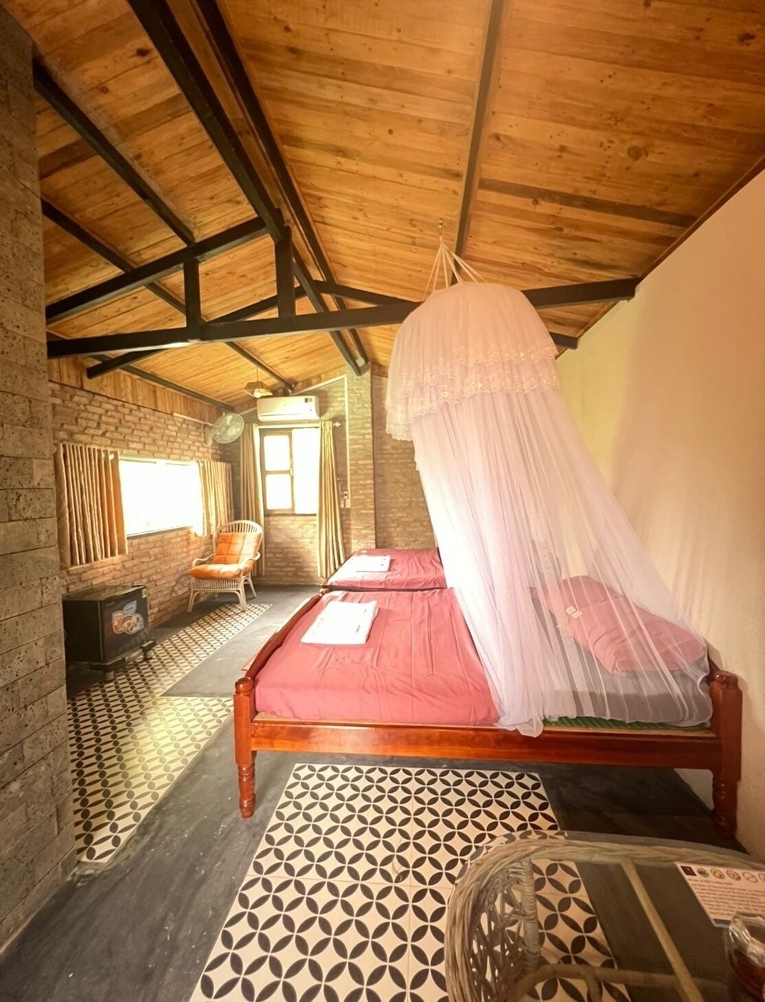 Une pièce avec deux lits, un plafond en bois, un mur en briques, un sol à motifs et une chaise.
