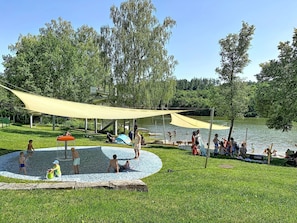 A park with a water play area, a covered seating area, and a lake.
