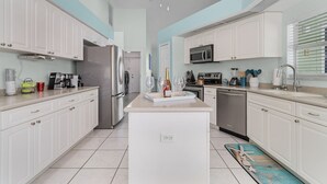 Una cocina moderna con armarios blancos, una isla central, electrodomésticos de acero inoxidable y suelo de baldosas.