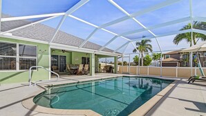 Un área de piscina con un porche cubierto, mobiliario exterior y vistas a casas vecinas.