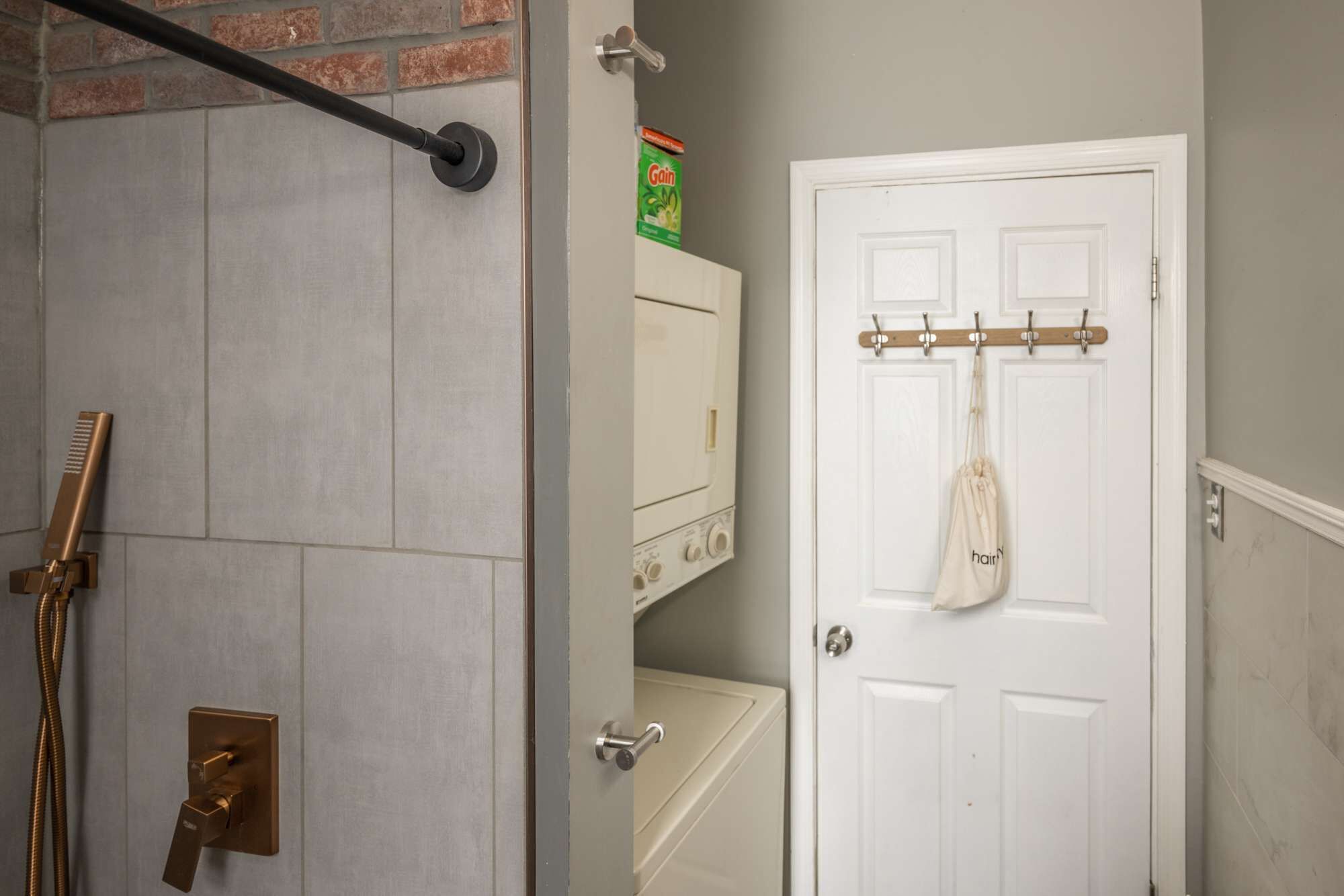 A bathroom with a shower, a toilet, and a white door with a coat rack.