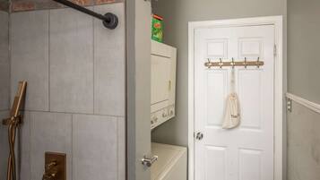 A bathroom with a shower, a toilet, and a white door with a coat rack.
