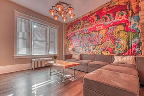 A living room with a large window, a sofa, a coffee table, and a colorful graffiti wall. - Historic Riverfront Steampunk Loft w/ River Views (Harrisburg)