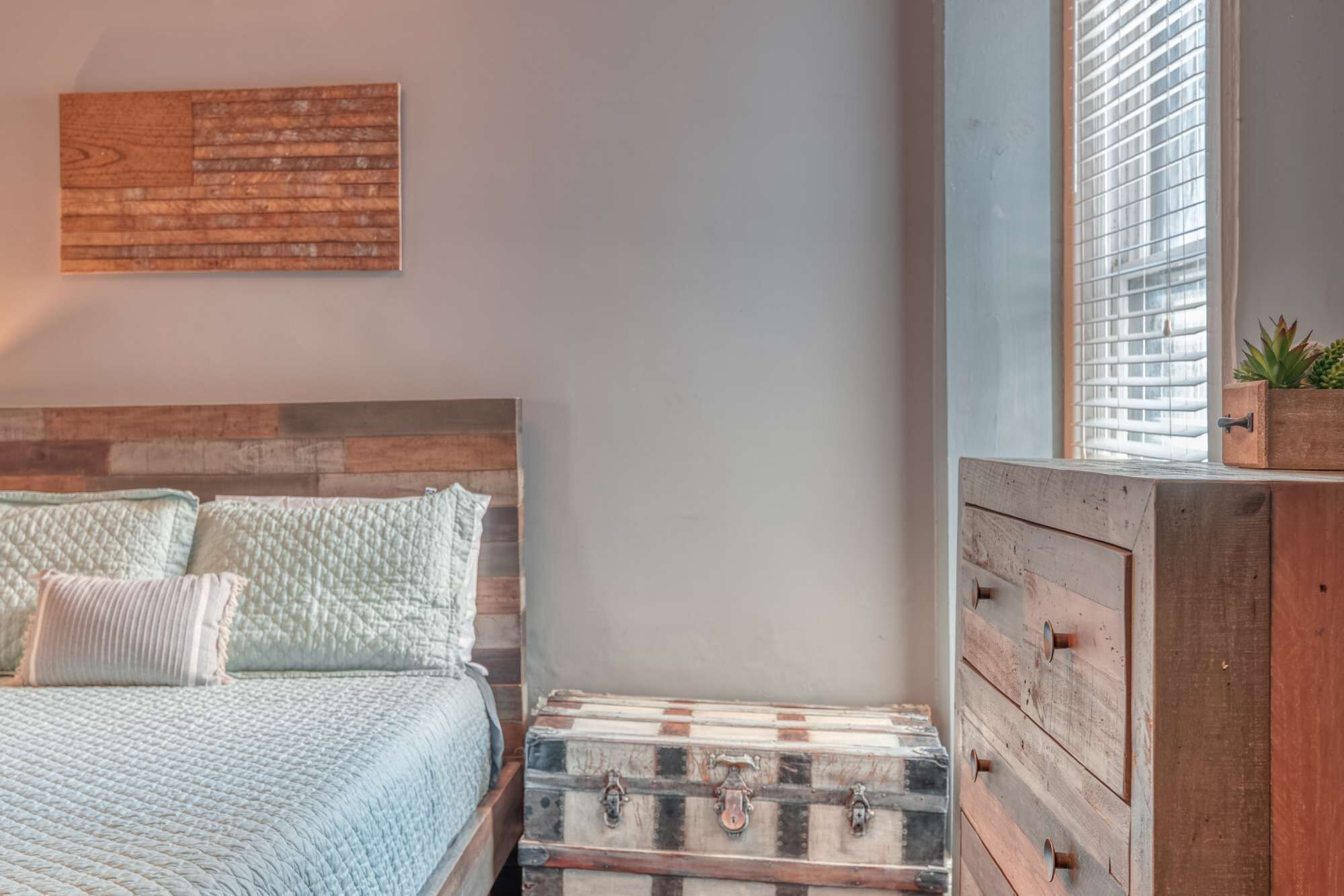 A bedroom with a wooden headboard, a bed with a quilted bedspread, and a chest of drawers with a vintage design.