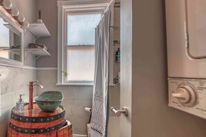 A bathroom with a wooden barrel sink, a mirror with lights, a window, and a shower curtain.