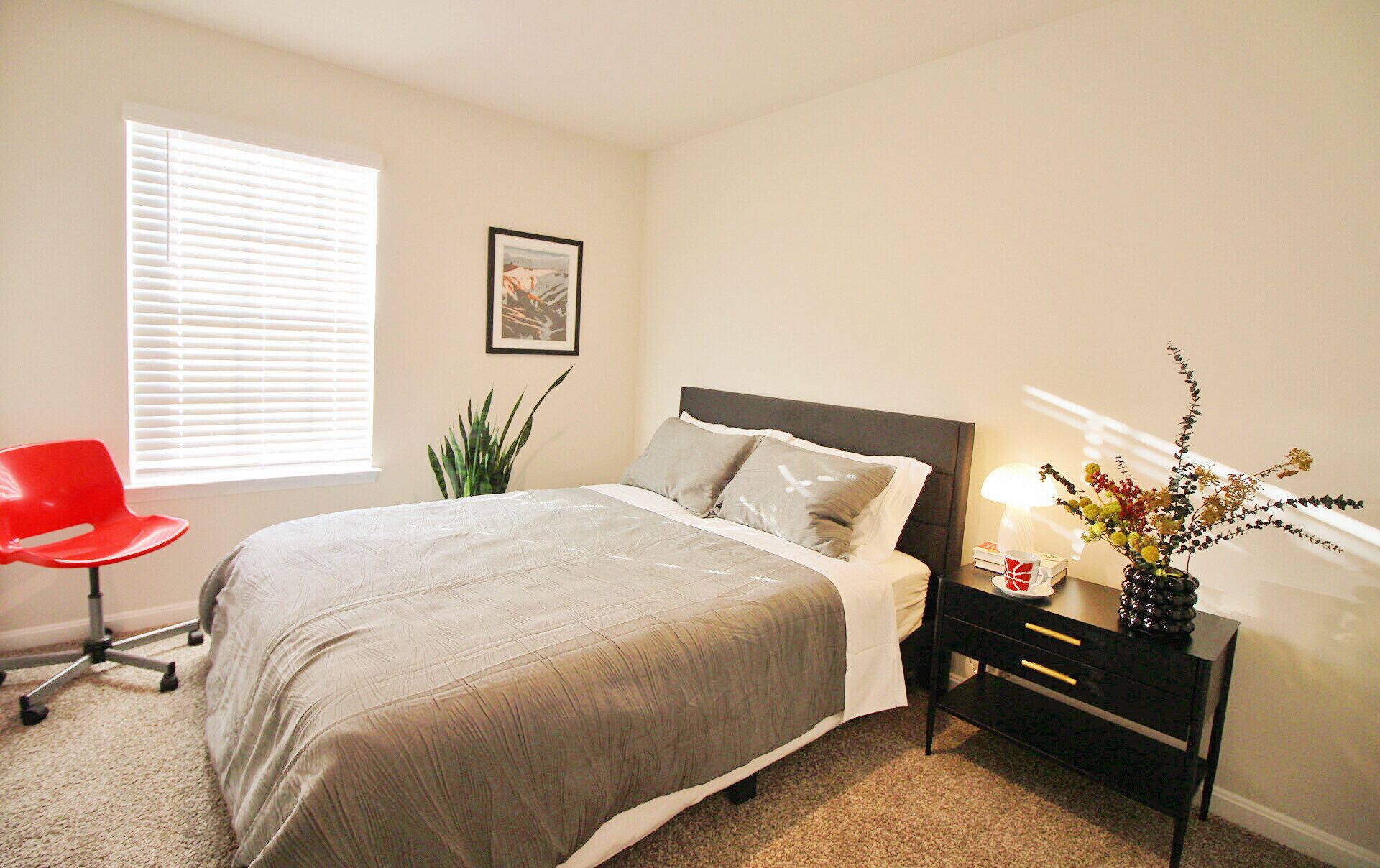 A neatly arranged bedroom with a bed, bedside table, lamp, and a potted plant.