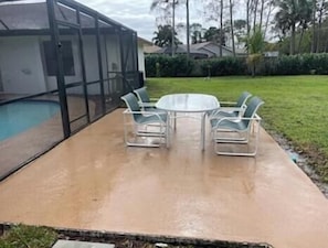 A covered patio area with a pool, a round table, and two chairs.