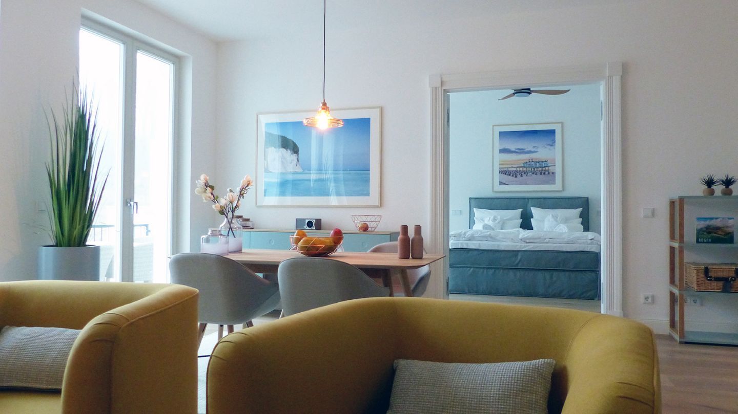 A modern hotel room with a bed, a dining area with a table and chairs, a large window, and a ceiling fan.
