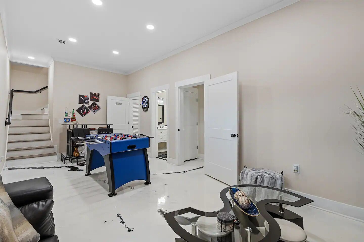 A spacious living area with a foosball table, a glass coffee table, and a staircase leading to another room.